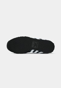Black sneaker sole with small square grip pattern, Adidas logo centered, and partial view of black and white striped upper.