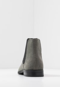 Bota de tornozelo em camurça cinza com painéis laterais elásticos e uma sola plana preta. O design apresenta um bico arredondado e uma textura suave.