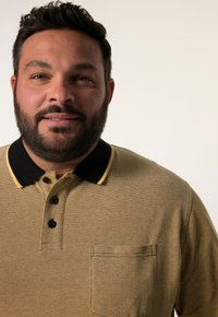 Hnědá texturovaná polo košile s černým límcem a žlutým akcentem. Obsahuje tři knoflíky a vyšitý kapesník na levé části hrudníku.