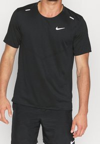 Camiseta atlética negra de Nike de manga corta con cuello redondo, que presenta detalles en blanco en los hombros y un pequeño logo en el pecho.