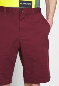 Shorts bordeaux in cotone con chiusura a bottone, tasche anteriori e dettagli di cucitura sulla orlo. Etichetta del marchio visibile sulla vita.
