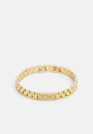 Gold-tone chain bracelet with rectangular plate featuring the word "GUESS" and surrounding small clear crystals.