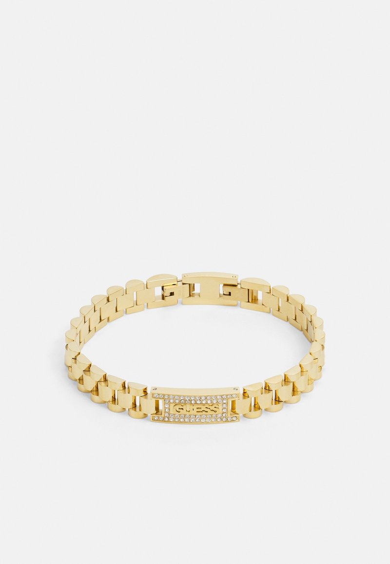 Bracelet chaîne en ton or avec plaque rectangulaire portant le mot "GUESS" et de petits cristaux clairs tout autour.