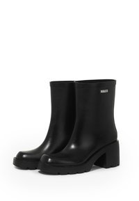 Black rubber ankle boots with a chunky heel, smooth texture, rounded toe, and a logo detail on the side. Treaded sole for grip.