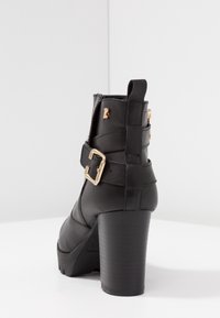 Sorte læder ankelstøvler med blokhæle, guldfarvet spænde og små gyldne dekorative detaljer på en glat hvid overflade.