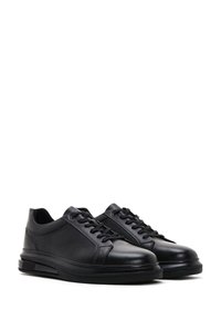Sneakers in pelle nera con lacci piatti, punta rotonda e suola spessa. Finitura liscia con sottili dettagli di cucitura laterale per una maggiore texture.