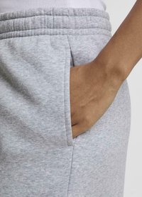 Tissu de sweat-shirt gris avec une texture douce, présentant une poche latérale et une taille élastique. Gros plan mettant en avant la poche et la main.