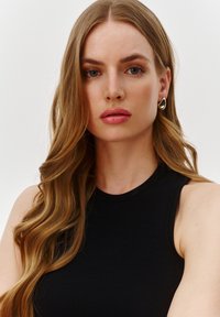 Czarny, prążkowany top bez rękawów z okrągłym dekoltem, noszony z złotymi kolczykami w kształcie łzy. Długie, falujące włosy dopełniają wygląd.