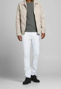 Ljusbeige mockajacka med två bröstfickor, strukturerad grå tröja, figurnära vita jeans och svarta snörskor. En jämn, avslappnad stil.