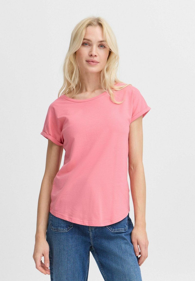 T-shirt rose à manches courtes avec un col rond et des manches retroussées, fabriquée en coton doux, associée à un jean bleu.
