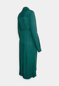 Vestuário verde de mangas longas, feito de tecido suave. Apresenta um decote com colarinho, uma cintura elástica e detalhes pregueados na parte de trás.