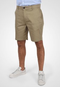 Pantalones cortos caqui de corte recto, con bolsillos frontales y cierre de un solo botón. Combinados con zapatillas blancas para un look casual.