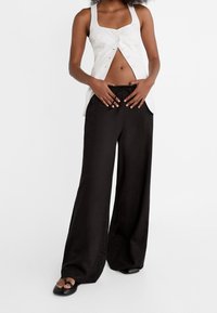 Biały lniany top z kwadratowym dekoltem i guzikami z przodu, w zestawieniu z czarnymi spodniami o szerokich nogawkach z regulowanym ściągaczem w talii.