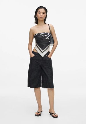 Femme portant un top bustier noir et blanc, un short rayé jusqu'aux genoux, des sandales à talons noires et un petit sac à main noir porté à l'épaule.