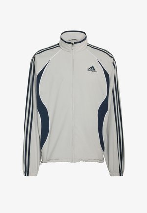 Veste zippée gris clair avec des accents bleu marine, présentant trois rayures sur les manches et un logo Adidas sur le haut à gauche. Texture de tissu lisse.