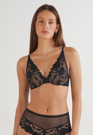 Zwarte kanten bralette met een bloemenontwerp, V-halsvorm, verstelbare bandjes en bijpassende sheer polkadot-slips met kantdetails.