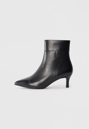 Bottine noire en cuir à bout pointu avec un talon moyen fin et un détail de poignet plié sur fond blanc uni.