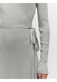 Grijze geribbelde gebreide jurk met lange mouwen, wikkeldesign en strik in de taille; heeft een verticale ribbeltextuur en uitlopende mouwuiteinden.