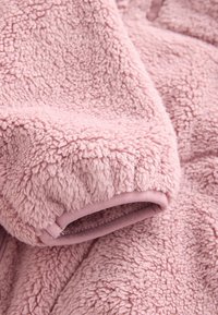 Light pink fleece garment featuring a soft, textured surface, with a smooth, solid-colored trim at the cuff and hem.