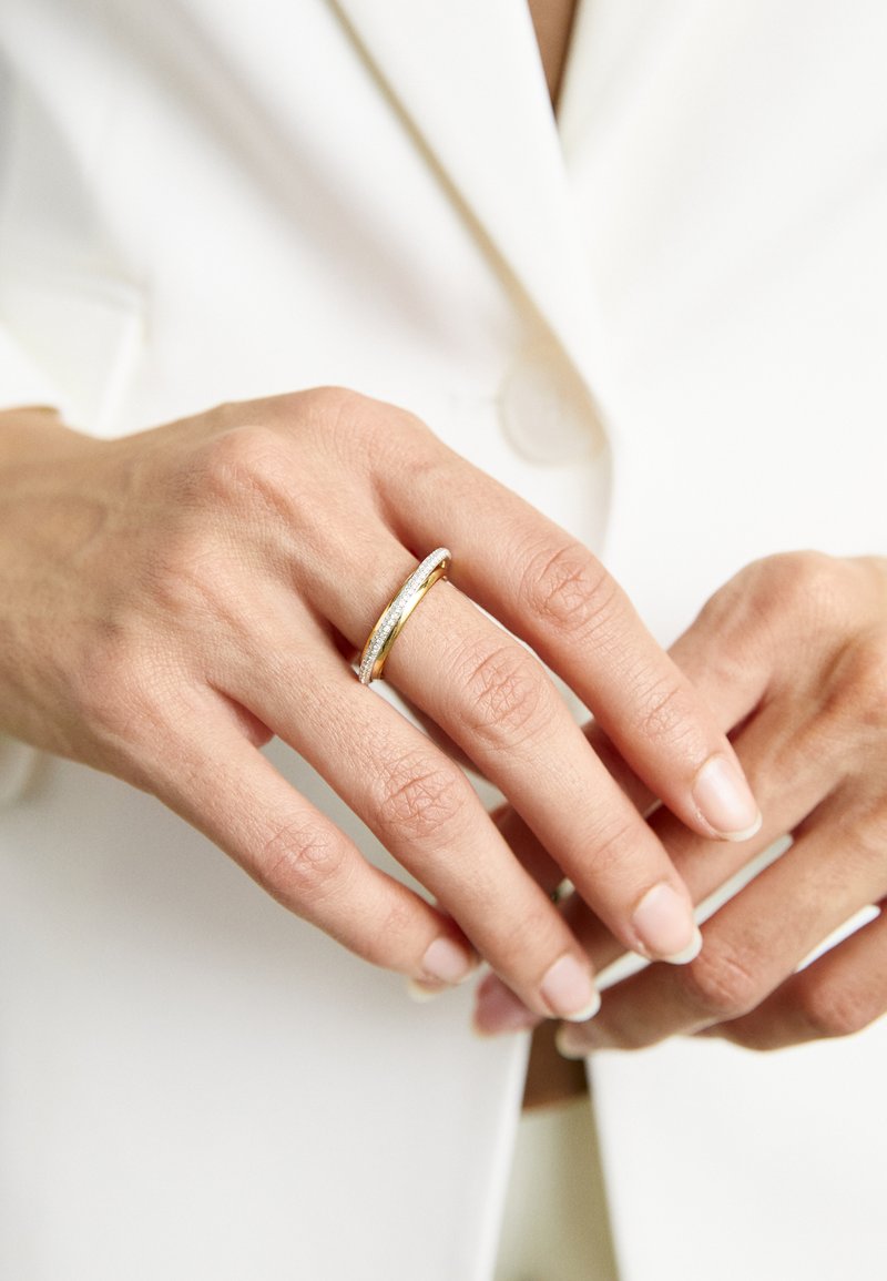 Zlato in srebro dual-band prstan na roki z naravnimi nohti, s svojo gladko, teksturirano končavo in sleek oblikovanjem.