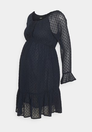 Rochie de maternitate de un albastru închis, cu textură punctată, mâneci lungi dintr-un material transparent, decolteu rotund și margine fului cu volane. Material ușor, fluid.