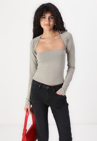 Långärmad, figurnära topp i ljusgrått tyg med fyrkantig halsringning och slät textur, kombinerad med högmidjade svarta jeans och en röd väska.