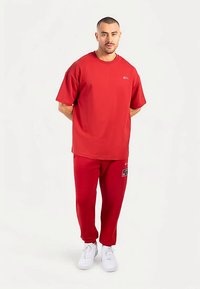 Camiseta de algodón roja con cuello redondo y mangas cortas, combinada con pantalones deportivos rojos que tienen un parche con logo y zapatillas blancas.