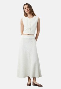 Valkoinen teksturoitu crop-top, jossa on pyöreä kaula-aukko ja etupainikkeet, yhdistettynä pitkään vastaavaan hameeseen, jossa on kohokuvioituja kukkakuvioita.