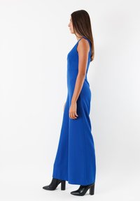 Jumpsuit blu royal con corpino aderente e pantaloni a gamba larga. Abbinato a stivali neri con tacco alto. Tessuto liscio, design senza maniche.