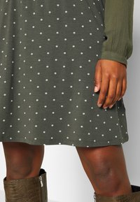 Robe verte en tissu doux avec des pois blancs, à manches longues et à coupe décontractée, associée à des bottes chevilles marron texturées.