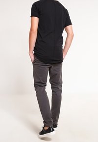 Czarna koszula z krótkim rękawem, dopasowany fason z detalami wzdłuż szwu z tyłu, zestawiona z szarymi spodniami o wąskim kroju oraz czarnym obuwiem z białymi podeszwami.