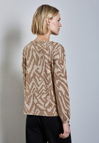 Braun gemusterter Pullover mit langen Ärmeln, der aus einem strukturierten Stoff besteht und ein abstraktes Design in hellen Cremetönen aufweist. Rundhalsausschnitt.