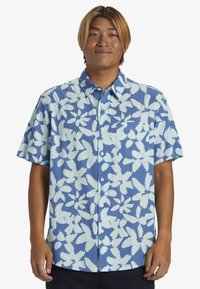 Camicia a maniche corte con bottoni, caratterizzata da uno sfondo blu con motivi floreali bianchi e una tasca sul petto. Realizzata in tessuto leggero.