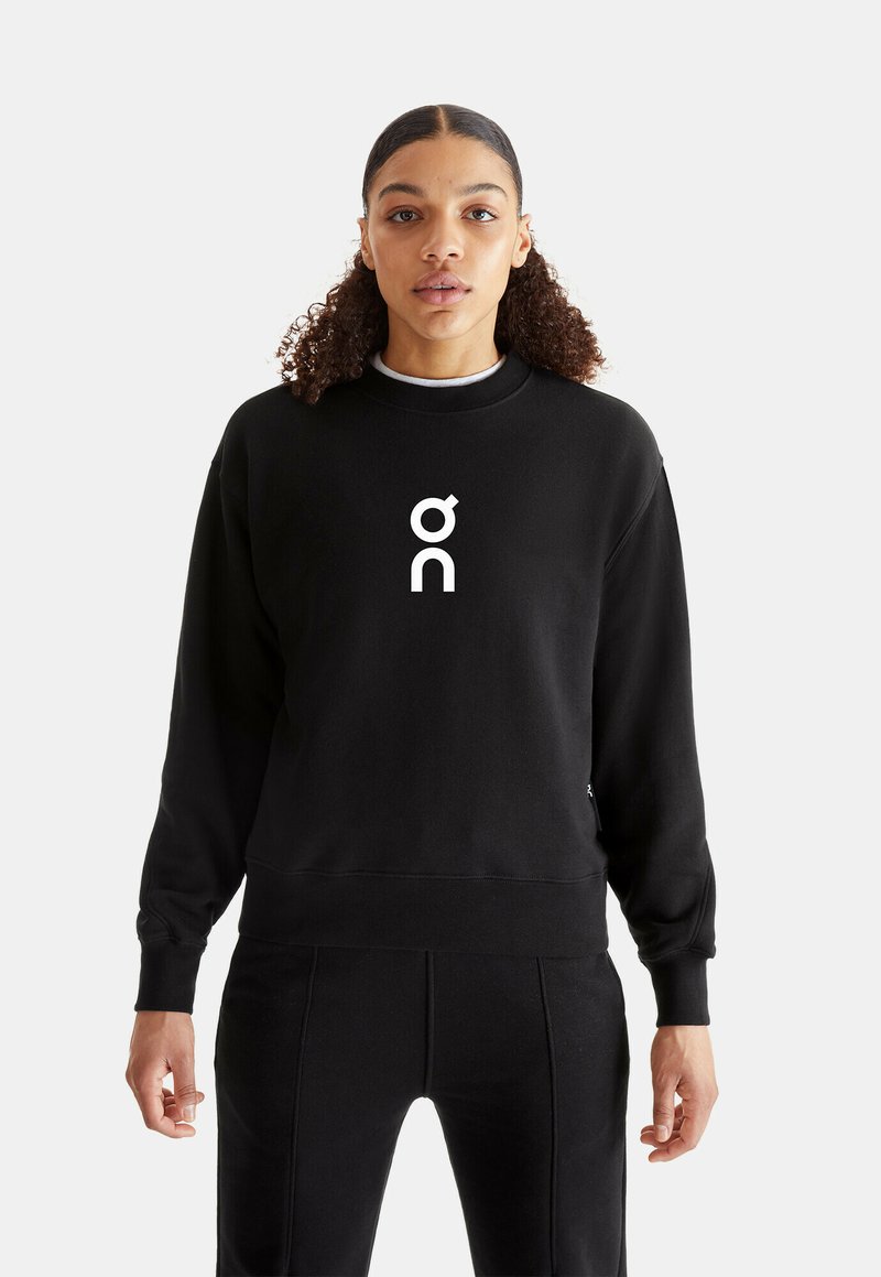 Black sweatshirt features a crew neck, long sleeves, and the white logo "on" centered on the front. Fabric appears soft and smooth.