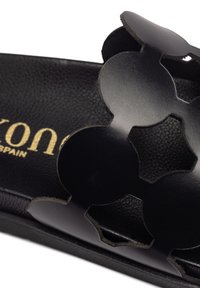 Sandale en cuir noir avec un motif circulaire découpé, semelle plate et semelle intérieure texturée. Logo embossé en or sur la bride.