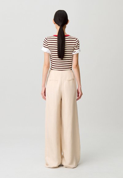 Top a maglia a righe con maniche corte, abbinato a pantaloni beige a gamba larga con righe verticali e tasche posteriori.