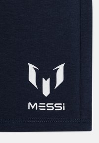 Náměsíčná tmavě modrá tkanina s hladkou texturou, na které je bílé logo nad textem "MESSI" tučným písmem. Jednoduchý a moderní design.