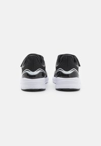 Baskets de sport noires avec une tige en mesh texturé, des accents brillants et une semelle intermédiaire blanche. Présente un motif ondulé blanc contrastant à l'arrière.