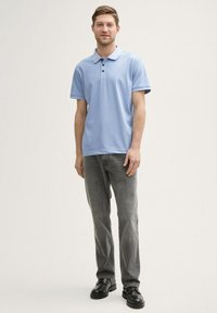 Ljusblå polo skjorta med krage och tre knappar, kombinerad med grå jeans och svarta skor. Rakt snitt med korta ärmar.