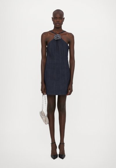 Denim halterklänning i mörkblått med en rosaccent vid halsringningen. Tillbehör inkluderar en liten väska med silverkedja och svarta klackar.