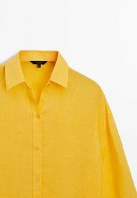 Chemise en lin jaune avec un col pointu, une patte de boutonnage et des manches courtes. Présente un tissu texturé avec une coupe décontractée.