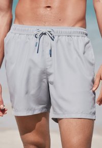 Lichtgrijze zwemshorts met een elastische tailleband, verstelbare trekkoord, zijzakken en een gladde, lichtgewicht stoftextuur.