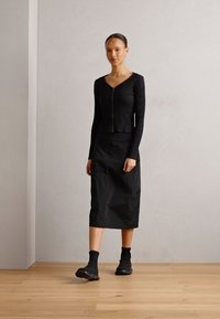 Top negro de manga larga con textura acanalada y cremallera frontal, combinado con una falda de longitud media y elegantes botas negras de tobillo. Diseño y textura minimalistas.