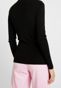 Pull noir à manches longues avec une coupe ajustée et une texture côtelée, assorti à un pantalon côtelé rose pâle. Coutures visibles et détails subtils.
