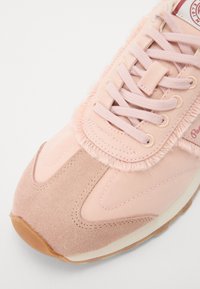 Rosa sneakers med semsket og tekstil overdel, med en fluffy krage, flate snører og gummisåle. Rund tå og kontrasterende teksturer.
