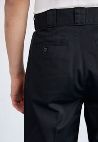 Pantaloni neri su misura con una texture liscia, dotati di una tasca posteriore con bottone e di una vita piatta, che mostrano un design pulito e semplice.