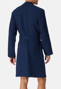 Accappatoio blu navy in tessuto a nido d'ape, con maniche lunghe, colletto e cintura, caratterizzato da un taglio fino al ginocchio e una tasca laterale.