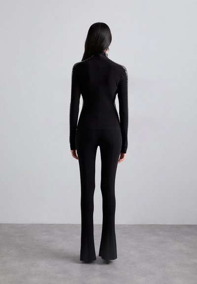 Sort træningsoutfit bestående af en langærmet top med høj krave og flagrende bukser, begge med teksturerede accentdetaljer langs siderne.