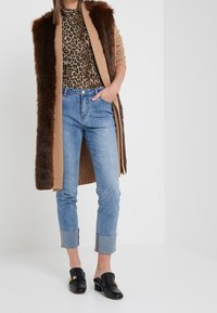 Hnědá umělá kožená vesta přes top s leopardím potiskem, spárovaná se světle modrými manžetovými džíny a černými muly se zlatým akcentem.