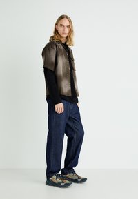 Chemise à manches courtes dégradée brune sur un long haut noir, associée à un pantalon large bleu foncé et des baskets multicolores.